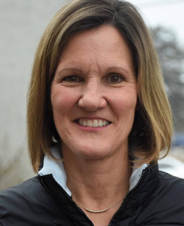 Person with shoulder-length hair smiles while wearing a black jacket.