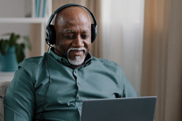 Smiling man with headphones sits on a couch using a laptop in a cozy room.