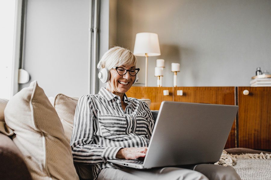 woman with white hair at home looking at laptop with headphones on.