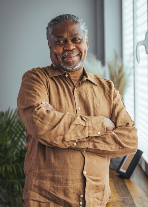 Smiling man in a brown shirt stands in home living room.